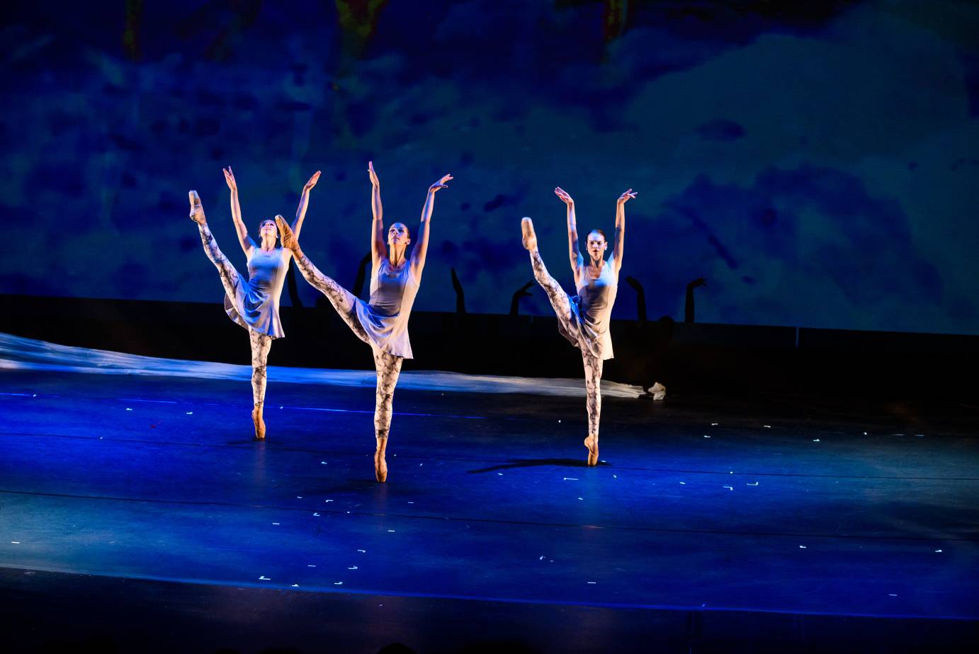 Three dancers extend a leg skyward, their arms in a V